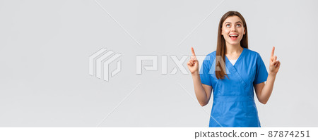 Healthcare workers, prevent virus, covid-19 test screening, medicine concept. Cheerful smiling pretty female doctor or nurse in blue scrubs, pointing fingers up and looking up rejoicing 87874251