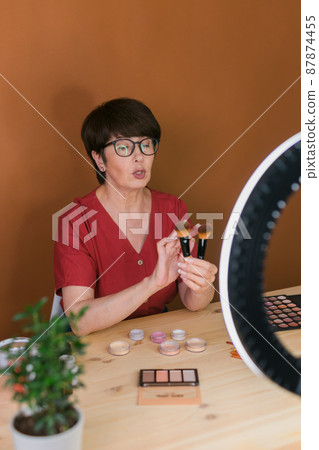 Beauty and cosmetics e-commerce and blogging concept - professional mature female make up artist testing new cosmetics recording video review on cosmetic products at home Beauty and cosmetics e-commerce and blogging concept - professional mature female make up artist testing new cosmetics recording video review on cosmetic products at home 87874455