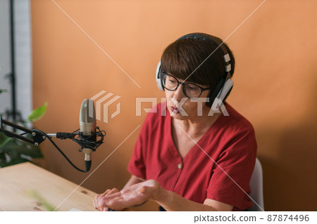 Portrait of mature woman wearing headphones and talking at online radio station - podcast and broadcast concept Portrait of mature woman wearing headphones and talking at online radio station - podcast and broadcast concept 87874496