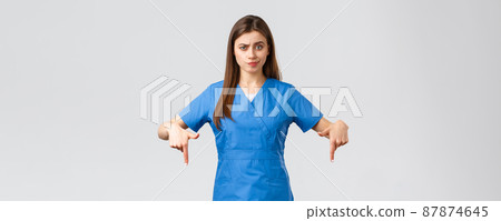Healthcare workers, prevent virus, covid-19 test screening, medicine concept. Skeptical, disappointed female nurse or doctor in blue scrubs pointing fingers down, smirk unsatisfied, being doubtful Healthcare workers, prevent virus, covid-19 test screening, medicine concept. Skeptical, disappointed female nurse or doctor in blue scrubs pointing fingers down, smirk unsatisfied, being doubtful 87874645
