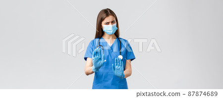 Covid-19, preventing virus, health, healthcare workers concept. No thank you. Displeased and reluctant female nurse or doctor in medical mask and scrubs, make stop, rejection or refusal sign 87874689