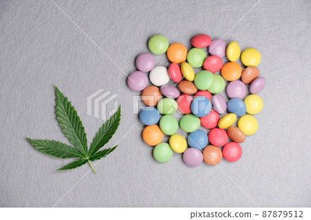 Modern cannabis kitchen. Marijuana leaf with colorful candy confetti on gray background close up 87879512