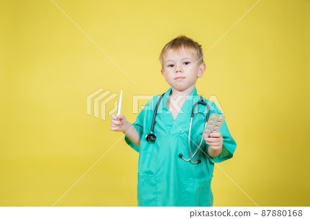 Portrait of little caucasian boy dressed in doctors coat holds pills 87880168