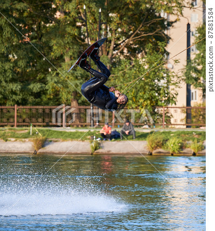 Wakeboarder making tricks while wakeboarding on lake. Young man surfer having fun wakesurfing in the cable park. Water sport, outdoor activity concept. 87881584