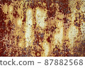 Brown abstract background with beige orange red hues. A weathered, rust-eaten textured sheet of metal with traces of paint residue. 87882568