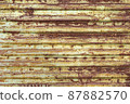 Red brown abstract background with pink and beige shades. A rust-eaten ribbed textured sheet of metal with remnants of paint marks. 87882570