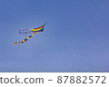 A kite painted in the colors of a rainbow flies against the background of a blue sky. 87882572