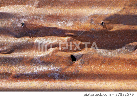 Brown abstract background with silver red hues. A weathered, rust-eaten, crumpled, perforated textured sheet of metal. Brown abstract background with silver red hues. A weathered, rust-eaten, crumpled, perforated textured sheet of metal. 87882579