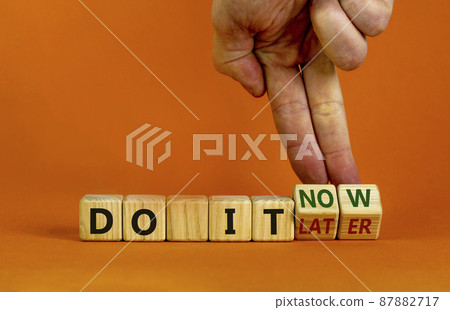 Do it now symbol. Businessman hand turns cubes and changes words 'do it later' to 'do it now'. Beautiful orange background. Business and do it now concept. Copy space. Do it now symbol. Businessman hand turns cubes and changes words 'do it later' to 'do it now'. Beautiful orange background. Business and do it now concept. Copy space. 87882717