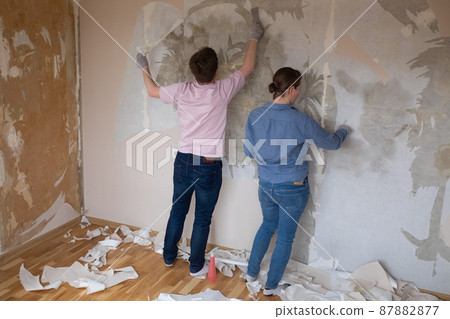 Young couple removing old wallpaper from walls preparing for flat renovation. Young couple removing old wallpaper from walls preparing for flat renovation. 87882877