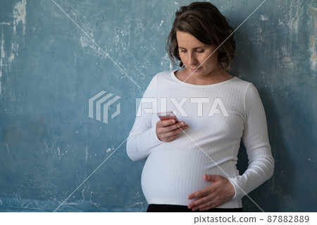 Pregnant woman talking on phone holds smart phone, touching her belly, consults with somebody 87882889