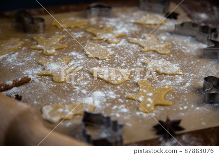 There are ready-made cookies of different shapes on the parchment, a rolling pin, cookie cutters and a sieve with flour are lying nearby, flour is scattered everywhere. High quality photo 87883076