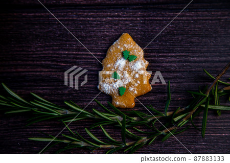 Cookies in the form of a Christmas tree, sprinkled with powdered sugar and small Christmas trees on top, lies on a dark wooden background surrounded by grained rosemary. High quality photo Cookies in the form of a Christmas tree, sprinkled with powdered sugar and small Christmas trees on top, lies on a dark wooden background surrounded by grained rosemary. High quality photo 87883133