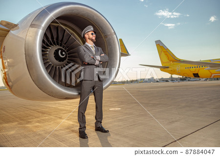 Cheerful airline captain standing near turbine engine at airport 87884047