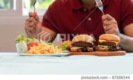 Young Man holding knife and fork are ready to eating a hamburger, French fries, and Spaghetti for Lunch. Concept of binge eating disorder (BED) and Relaxing with Eating junk food and unhealthy foods. Young Man holding knife and fork are ready to eating a hamburger, French fries, and Spaghetti for Lunch. Concept of binge eating disorder (BED) and Relaxing with Eating junk food and unhealthy foods. 87886544