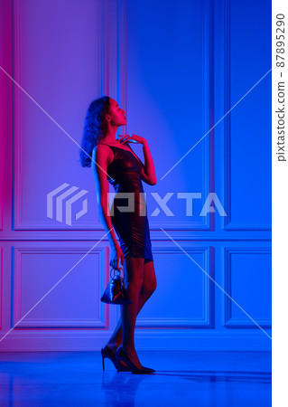 african american model in eco leather dress, fishnet tights with hand bag under neon lights 87895290