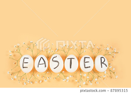 White eggs with black letters EASTER around Gypsophila flowers on yellow background. 87895315