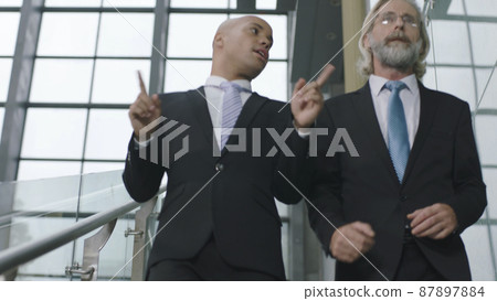 two corporate executives talking while descending stairs in modern office building 87897884