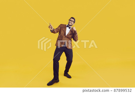 Happy young black man in party outfit dancing isolated on yellow colour background. Full length shot of positive guy in leopard jacket, bowtie and glasses enjoying music and having fun in the studio Happy young black man in party outfit dancing isolated on yellow colour background. Full length shot of positive guy in leopard jacket, bowtie and glasses enjoying music and having fun in the studio 87899532