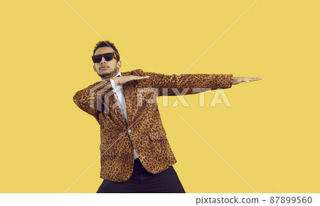 Funny young black man dancing isolated on a yellow colour background. Confident ethnic guy wearing a leopard jacket and cool sunglasses dancing to hip hop music in the studio Funny young black man dancing isolated on a yellow colour background. Confident ethnic guy wearing a leopard jacket and cool sunglasses dancing to hip hop music in the studio 87899560