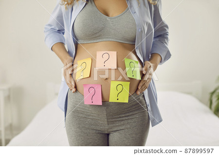 Choosing baby name. Cropped image of pregnant woman with many colored stickers on her abdomen showing question marks. Woman wants to choose name and know sex of her unborn child. Expectancy concept. 87899597
