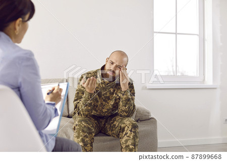 Sad upset depressed veteran soldier suffering from PTSD having therapy session with professional military psychologist, sitting on couch, thinking about horrors of war, sharing concerns and worries 87899668