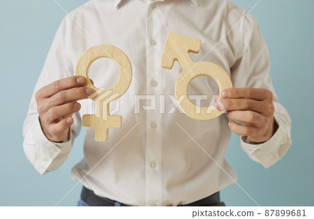 Close up of male and female gender symbols in human hands. Young man holding heterosexual couple symbols: Venus mirror and Mars arrow. Sexuality, attraction to opposite sex, love, relationship concept 87899681