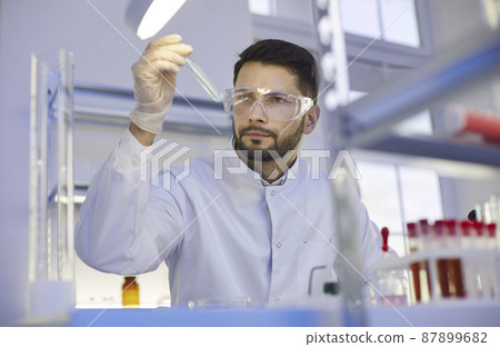 Young Caucasian man in white medical uniform and glasses do laboratory experiments with test tube. Male assistant do chemistry investigation research in lab. Biotechnology, science concept. Young Caucasian man in white medical uniform and glasses do laboratory experiments with test tube. Male assistant do chemistry investigation research in lab. Biotechnology, science concept. 87899682