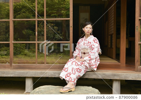 A young and beautiful woman in a yukata sitting on the porch of an old folk house and smiling A young and beautiful woman in a yukata sitting on the porch of an old folk house and smiling 87900086
