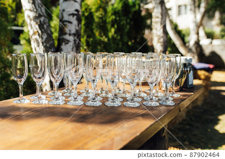 Row of empty champagne glasses on a table outdoors with sun reflection. Selective focus. Celebration concept 87902464