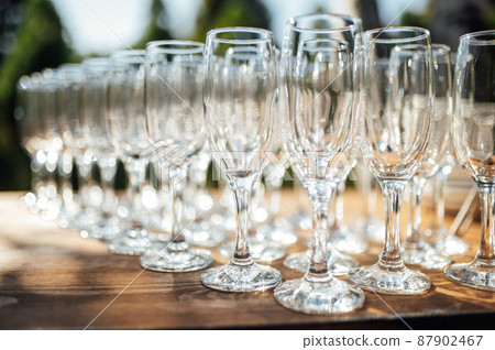 Row of empty champagne glasses on a table outdoors with sun reflection. Selective focus. Celebration concept Row of empty champagne glasses on a table outdoors with sun reflection. Selective focus. Celebration concept 87902467