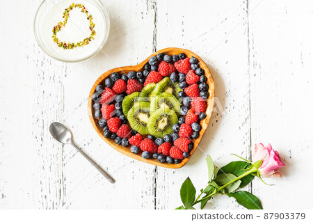 S.Valentine's Day breakfast concept. Mix of berries and kiwi in a heart shaped bowl, yogurt with pistachios and rose S.Valentine's Day breakfast concept. Mix of berries and kiwi in a heart shaped bowl, yogurt with pistachios and rose 87903379