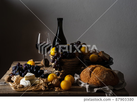 Still life with red wine, black grape, cheese, bread, yellow plums and nuts in old fashioned rustic style.  87903380