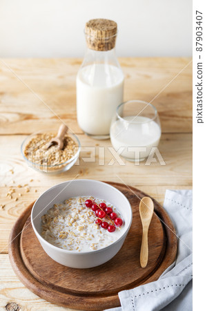 Healthy milky porridge from whole hulled grain oats with oat milk and red currant berries in bowl 87903407