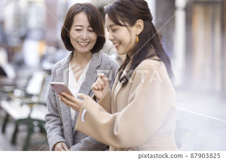 一個穿著外套，看著智能手機的女人 父母和孩子 母女 87903825