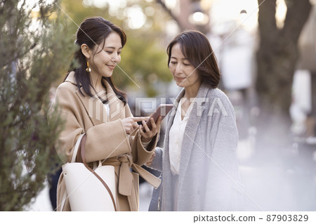 A woman wearing a coat and looking at a smartphone Parent and child Mother and daughter 87903829