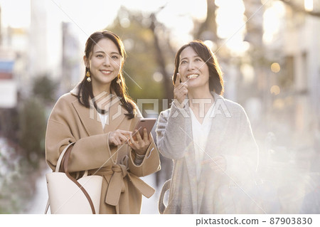 A woman wearing a coat and looking at a smartphone Parent and child Mother and daughter 87903830