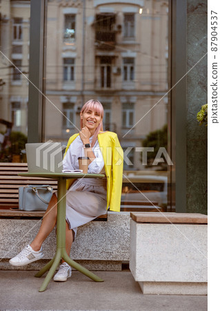Cheerful woman sitting at the table with laptop on the street Cheerful woman sitting at the table with laptop on the street 87904537