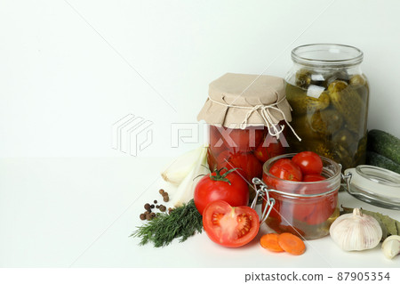 Jars of pickled vegetables and ingredients on white table 87905354