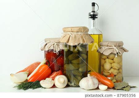 Jars of pickled vegetables and ingredients on white table 87905356