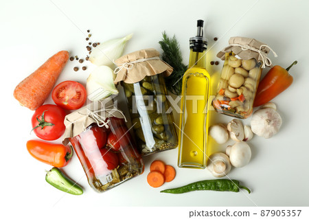 Jars of pickled vegetables and ingredients on white table 87905357