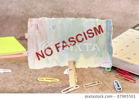 no fascism text written on paper next to scattered paper clips, calculator, adhesive paper no fascism text written on paper next to scattered paper clips, calculator, adhesive paper 87905501