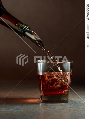 Whiskey is poured from a bottle into a frozen glass with natural ice. 87905550