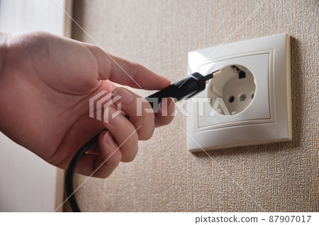 A female hand inserts an electric plug into a euro-format socket close-up 87907017