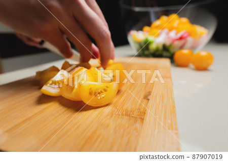 Sliced yellow cherry tomatoes on a wooden board in shallow depth of field against the background of a bowl with veggie salad ingredients Sliced yellow cherry tomatoes on a wooden board in shallow depth of field against the background of a bowl with veggie salad ingredients 87907019