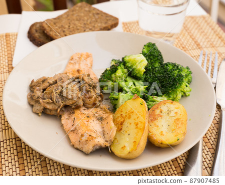 fried river trout fillet with a complex side dish of broccoli, baked potatoes and mushroom sauce 87907485