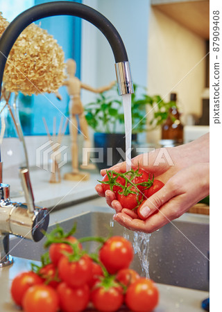 Woman washing tomato at kitchen sink 87909408