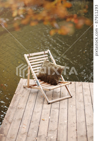Empty wooden dock on calm lake on cool cloudy fall day with lonely folding chair 87911293