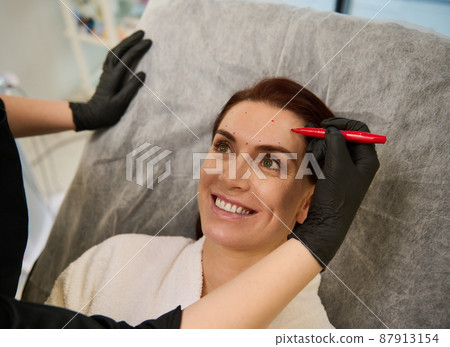 Cosmetologist drawing guidelines for cosmetic product injection. Thread facelift with arrows for middle aged woman skin, facial contouring procedure with meso threads for facial rejuvenation Cosmetologist drawing guidelines for cosmetic product injection. Thread facelift with arrows for middle aged woman skin, facial contouring procedure with meso threads for facial rejuvenation 87913154