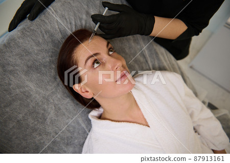 Attractive beautiful middle aged Caucasian woman receiving a beauty injection on her face in wellness spa clinic. Botulinum toxin and hyaluronic acid for skin smoothing and anti-wrinkles therapy 87913161